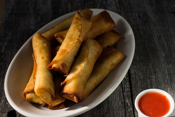 Homemade spring rolls with chinese sweet and sour sauce. In a white plate on a wooden background