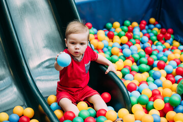 Obraz premium Happy laughing boy 1-2 years old having fun in ball pit in kids amusement park and indoor play center. Activity toys for little kid