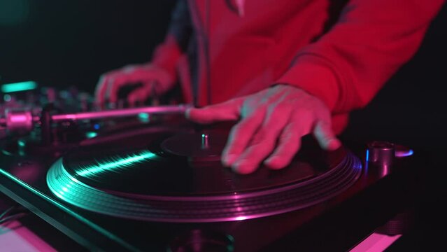 Party DJ scratches vinyl disc on turntable. Hip hop disc jockey scratching records and playing music in night club