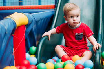 Happy laughing boy 1-2 years old having fun in ball pit  in kids amusement park and indoor play center. Activity toys for little kid