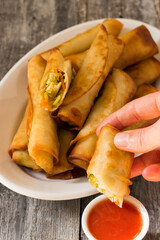 Woman's hand dipping homemade spring roll in Chinese sweet and sour sauce. White dish on a wooden background