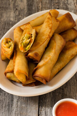 Homemade spring rolls with chinese sweet and sour sauce. In a white plate on a wooden background