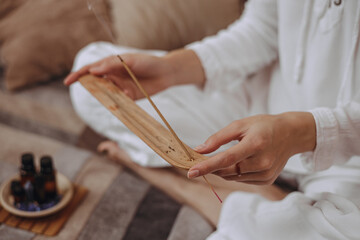 From above of crop woman with burning incense stick practicing yoga and enjoying aromatherapy at...