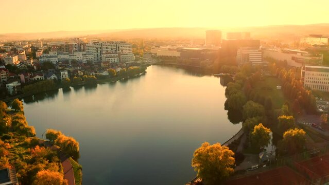 Cinematic, Establishing Aerial drone shot over Cluj-Napoca city, Iulius mall zone, Iulius park, lake view, sunrise. Reflective Park water.