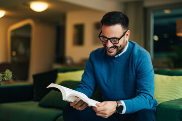 A smiling businessman reading a book, sitting at the home office.