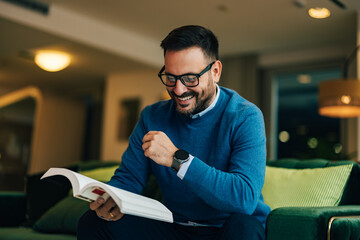 Adult businessman reading a book in the living room, wearing a watch.
