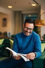 Smiling businessman reading a book and sitting on a comfortable couch.