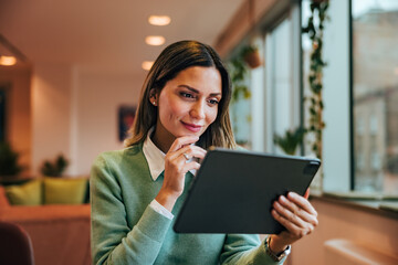 Businesswoman reading an online book over the digital tablet, smiling, elegantly dressed.