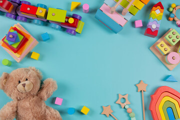 Baby kids toys frame background. Teddy bear, wooden educational stacking color recognition puzzle toys, wooden train and colorful blocks on light blue background. Top view, flat lay
