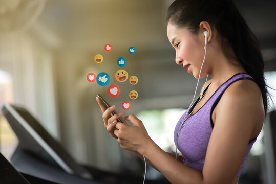 Asian woman enjoy using smartphone addiction to technology trends following with icons on social networks after exercise in gym. Social medias and technology concept. - Powered by Adobe
