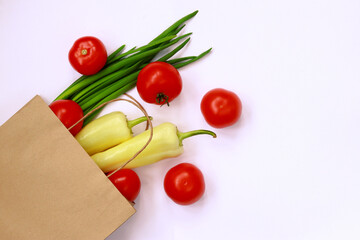 Healthy food is poured from a paper bag on a white background. Green onions, yellow peppers and ripe red tomatoes, healthy eating concept