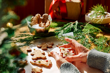 Woman's hands decorating glazed christmas gingerbread cookies a shape of gingerbread man,christmas tree and star,decorated with colorful sugared almonds.Christmas and New Year traditions festive food.