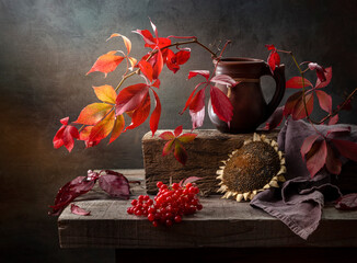 Rustic still life with a branch of wild grapes, viburnum and a sunflower