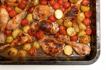 Homemade one-pan baked chicken with cherry tomatoes, baby potatoes and herbs in a metal dish on a white background. Top view