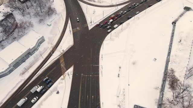 Top view of a winter city crossroads with cars, snow lies. Vehicles drive and stand at a traffic light. Regulated intersection, interchange. City of Vladimiro, Lybidskaya highway. UHD 4K.