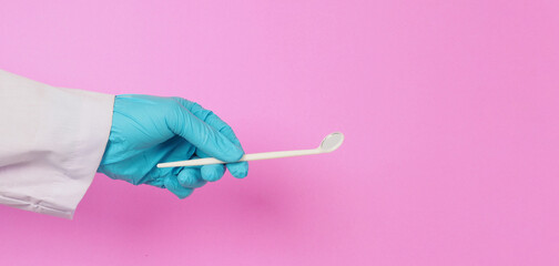 Dentist hand is hold Dental mirror on pink background. Hand wear blue latex glove.