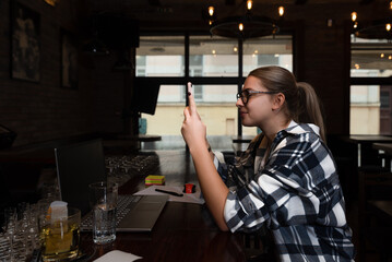 Young freelancer business woman sitting at the cafe bar in cafeteria working on her laptop computer, taking a break for her social media on her smartphone. Expert businessperson relaxing from work.  