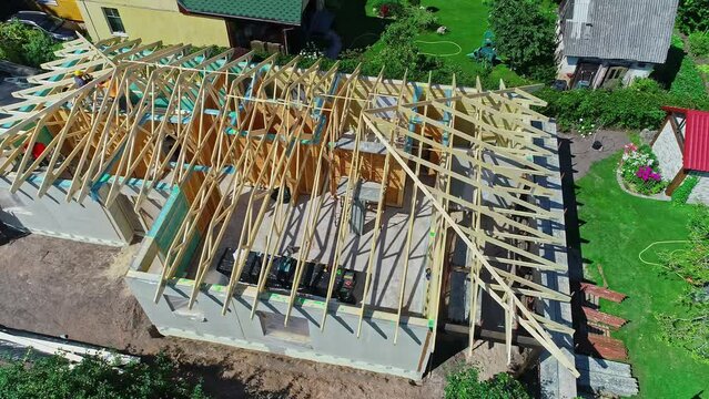 Aerial drone rotating shot over wooden frame of roof structure under construction in a suburban neighborhood on a bright sunny day.
