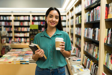 Happy woman reader carrying books and a coffee at the bookstore