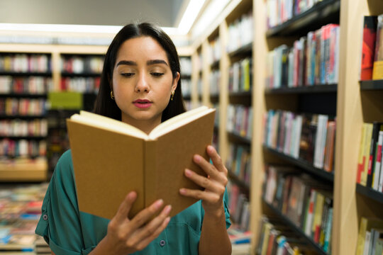Attractive reader woman enjoying a new novel at the book shop