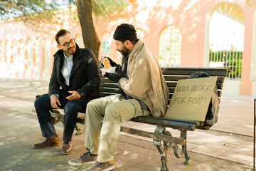 Caucasian man sitting with a poor homeless man on the bench