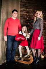 Beautiful young family in red having fun together for Christmas holidays, sitting on a living room floor next to a nicely decorated Christmas tree
