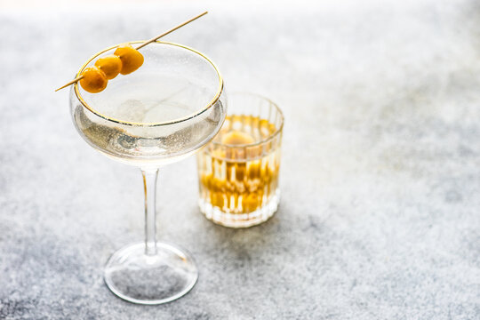Close-up of a vodka cocktail in an elegant cocktail glass and a glass of green cherries on a concrete table