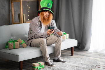Happy joyful shopper guy in leprechaun hat buying St.Patricks day gifts online, using smartphone,...