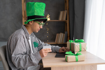 men wearing leprechaun hat sitting at table and using laptop and credit card to shopping online at...