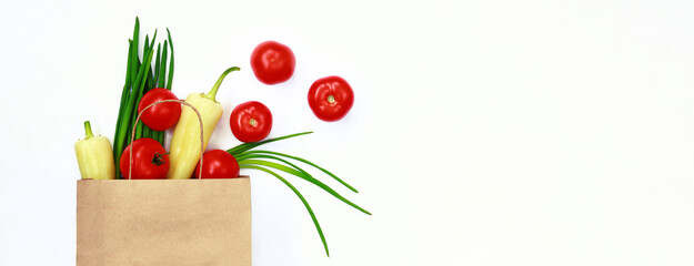 Vegetables are poured out of a paper bag on a white background, top view. The concept of healthy eating, shopping and ordering groceries at home with delivery. Tomatoes, green onions and peppers