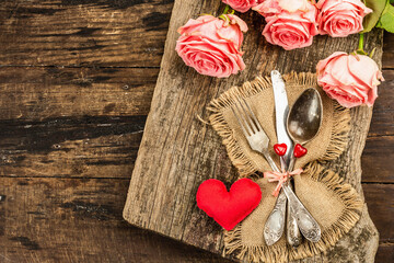 Rustic table setting for romantic dinner. Bouquet of fresh roses, cutlery and heart