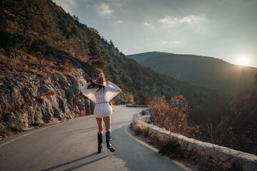 The woman is dear to the mountains. A woman in a white sweater, black boots and a hat walks along a winding alpine path between the mountains at the end of summer at sunset. Travel concept.