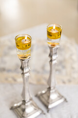 A pair of Shabbat candles are lit with oil on silver candlesticks on the Shabbat table.