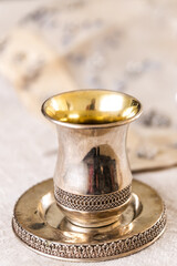 Traditional, decorative Jewish kiddush cup. Silver cup with saucer filled to the brim with purple wine isolated on a Shabbat table