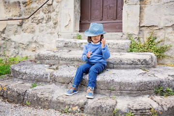 Little handsome baby boy sitting on ancient stone stairs and playing outdoor with straw hat in old city