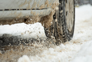 Close up of car wheel driving on melted snow. Winter thaw, mud on the road, cold season