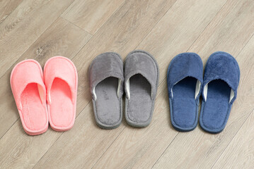 Top view of three pair of slippers on grey parquet. Warm male and female footwear for the house in cold periods