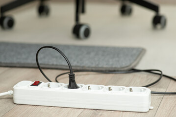 One black electric plug connects into white extension socket. Grey small carpet and wheels of an...