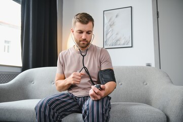 Young man measuring his blood pressure at home - obrazy, fototapety, plakaty