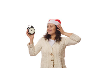 Delightful woman wearing Santa hat, holding black retro alarm clock with midnight on the clock...