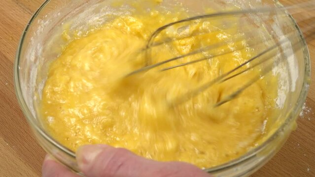 Liquid dough are whisking with wire wisk in a glass bowl in a glass bowl, making of the dough for baking