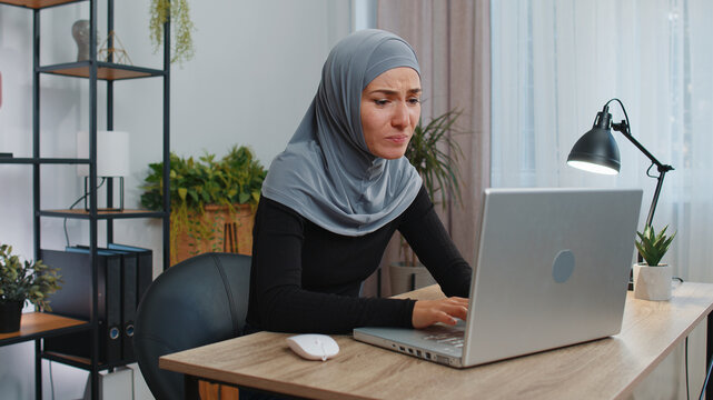 Business woman programmer software developer in hijab working on laptop loses becoming surprised sudden lottery results, bad news, fortune loss, fail at office. Concentrated freelancer muslim girl