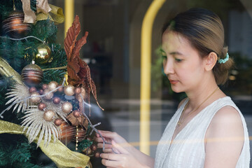 A joyful young woman is preparing for the Christmas holiday, decorating a Christmas tree in a cozy interior room of the house. Selective focus.