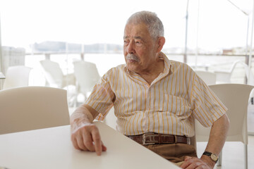  un signore anziano vestitocon camicia seduta al tavolino di un bar - obrazy, fototapety, plakaty