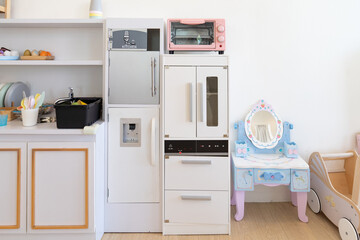 The full set of modern kitchen toys for kids such as microwave, stove, refrigerator and kitchen pantry and a make up table settled in a white playroom.