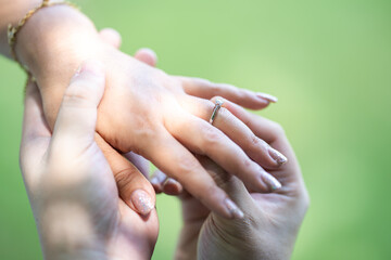 A man is wearing a wedding ring to a woman on his left ring finger. Close up on the hand in the outdoor field with the sunlight and tree shadow shading.