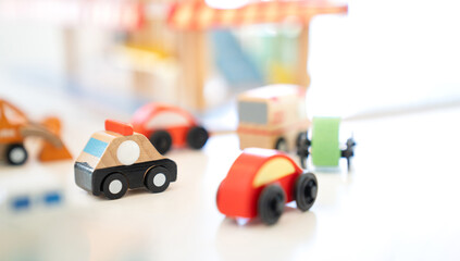 In an indoor playground, a wooden Police car toy drives behind in an Ambulance Van with a variety of cars trailing around it.