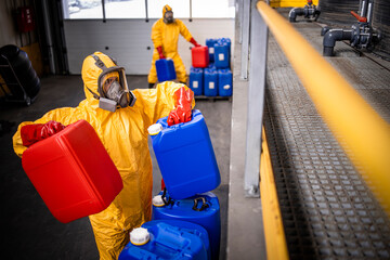 Chemical plant workers carrying plastic containers with chemicals or acids inside production factory.