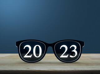 2023 white text with black eye glasses on wooden table over light blue wall, Business vision happy new year 2023 cover concept