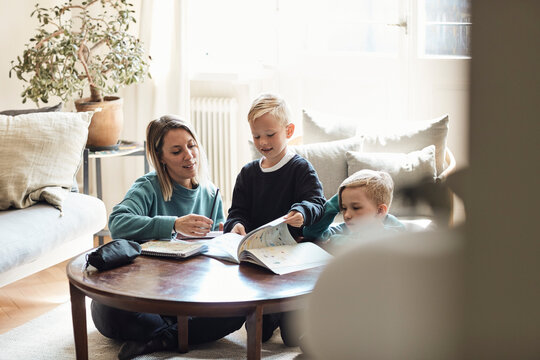 Mother sitting with sons while doing homework on table at home